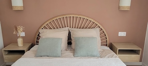 A bed with a wooden headboard, two bedside tables, and a vase with dried flowers on one side.