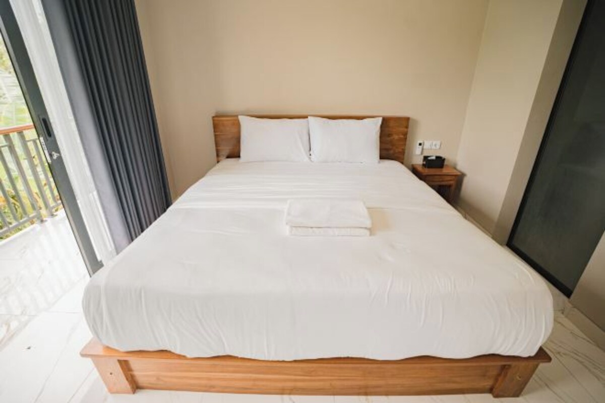 A hotel room with a large bed, a bedside table, and a view through a window.