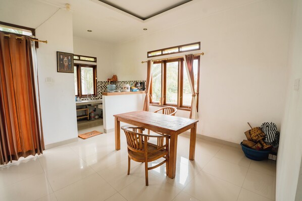 Un comedor con una mesa y sillas de madera, una cocina al fondo y una ventana con cortinas.