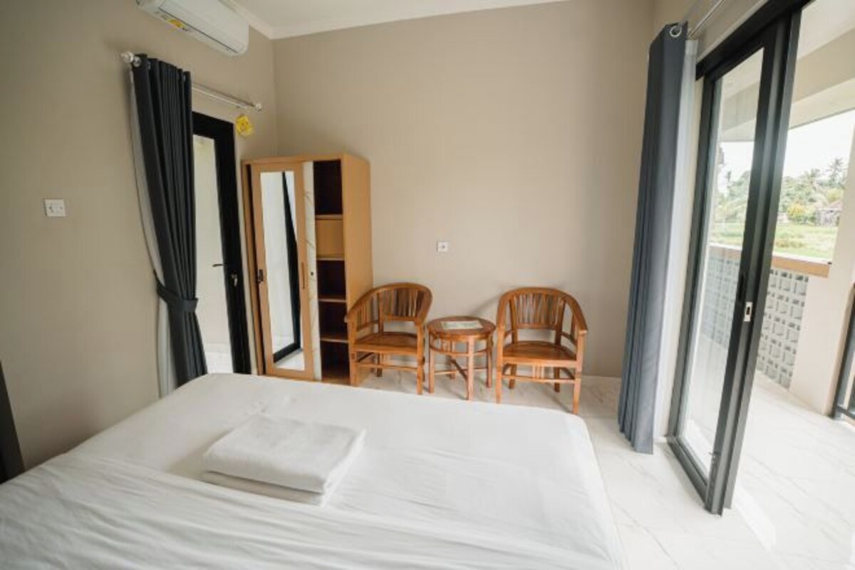 A hotel room with a bed, two chairs, a wardrobe, and a balcony.