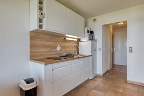 Una cucina moderna con mobili bianchi, un piano di lavoro in legno, un lavandino, un forno a microonde e un cestino.