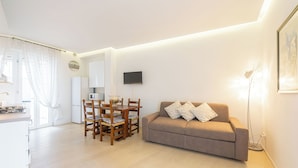 A modern living room with a sofa, a dining table with chairs, a flat-screen TV mounted on the wall, and a kitchen area with a refrigerator and microwave. - Casa Maria - vicino a Verona Centro (Verona)
