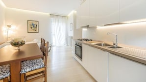 A modern kitchen with white cabinets, a gas stove, and a sink. There is a dining table with chairs and a vase of flowers. - Casa Maria - vicino a Verona Centro (Verona)
