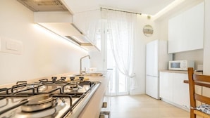 A modern kitchen with a gas stove, white cabinets, a microwave, and a wooden chair. - Casa Maria - vicino a Verona Centro (Verona)