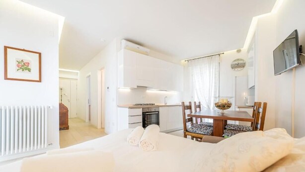 A bedroom with a bed, a dining table with chairs, a kitchen area, and a TV mounted on the wall. - Casa Maria - vicino a Verona Centro (Verona)