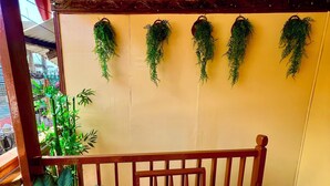 A wooden bench with a cushion, a potted plant, and hanging greenery against a yellow wall.