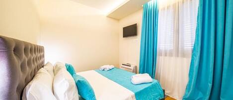 A hotel room with a bed, a flat-screen TV, and a window with curtains.