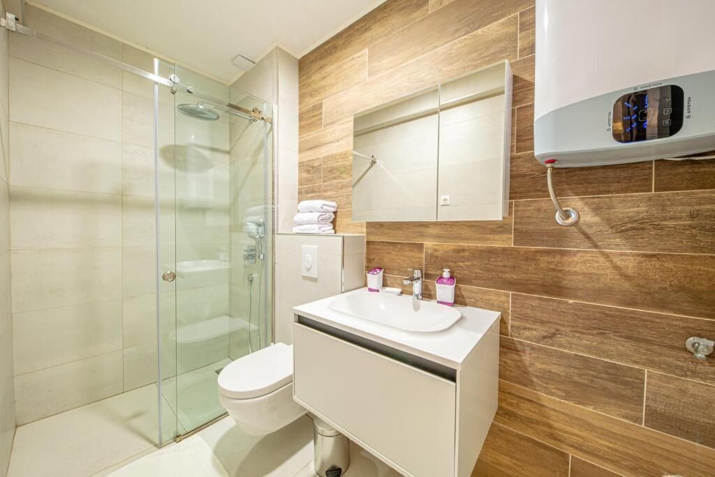 Een moderne badkamer met een glazen douchecabine, een witte wastafel en een houten spatwand.