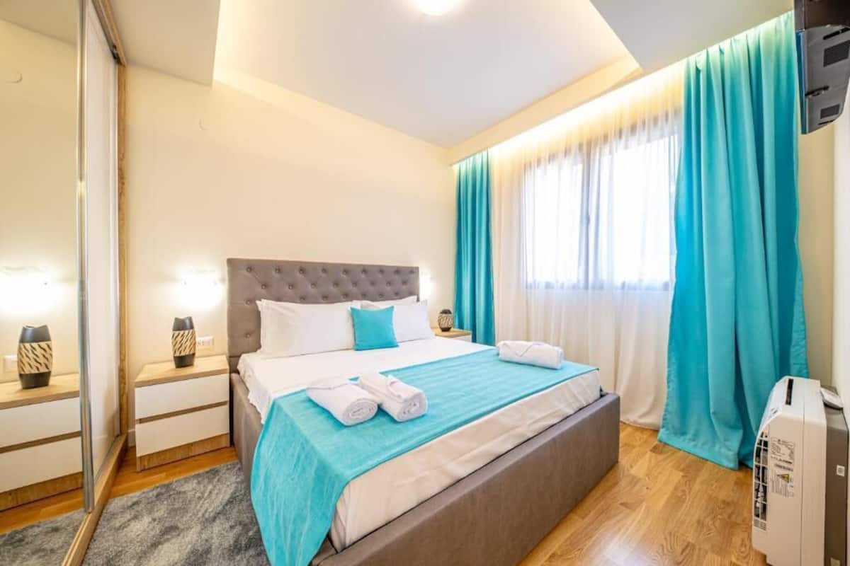 Una habitación de hotel con cama, mesitas de noche, un espejo, cortinas y un equipo de aire acondicionado.