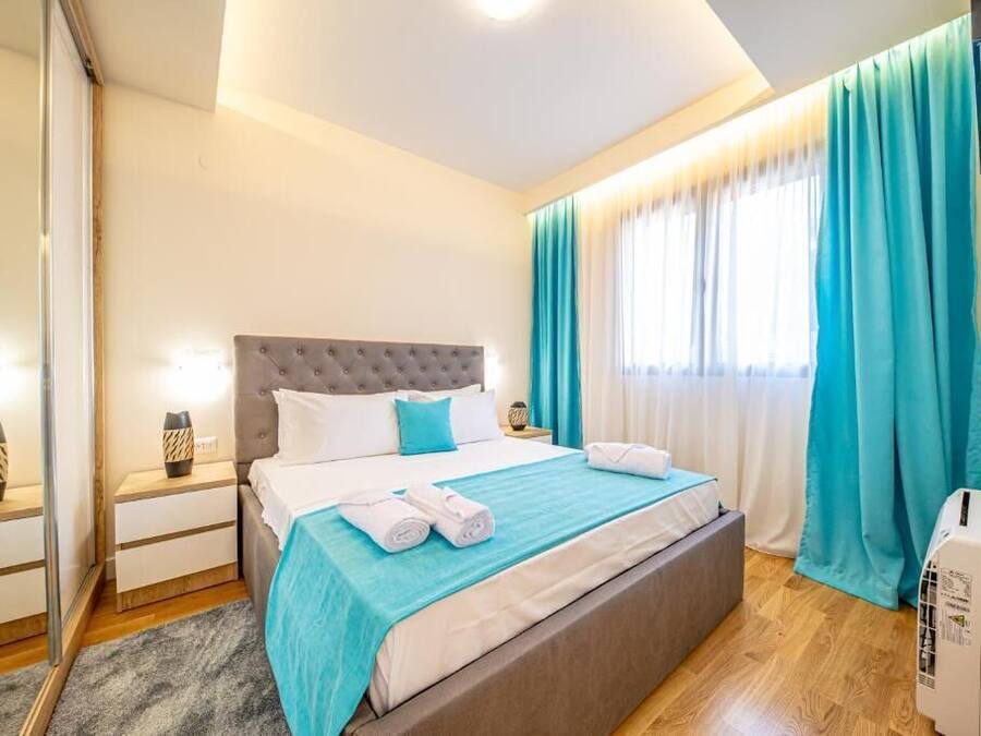 Una habitación de hotel con cama, mesitas de noche, un espejo, cortinas y un equipo de aire acondicionado.
