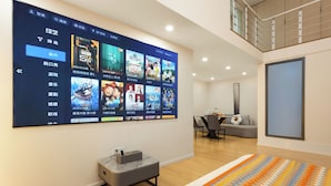 A modern living room with a large digital screen displaying movie posters, a gray ottoman, a colorful rug, and a dining area in the background. - The HEJINN House - Design Lofts & Suites (Chengdu)