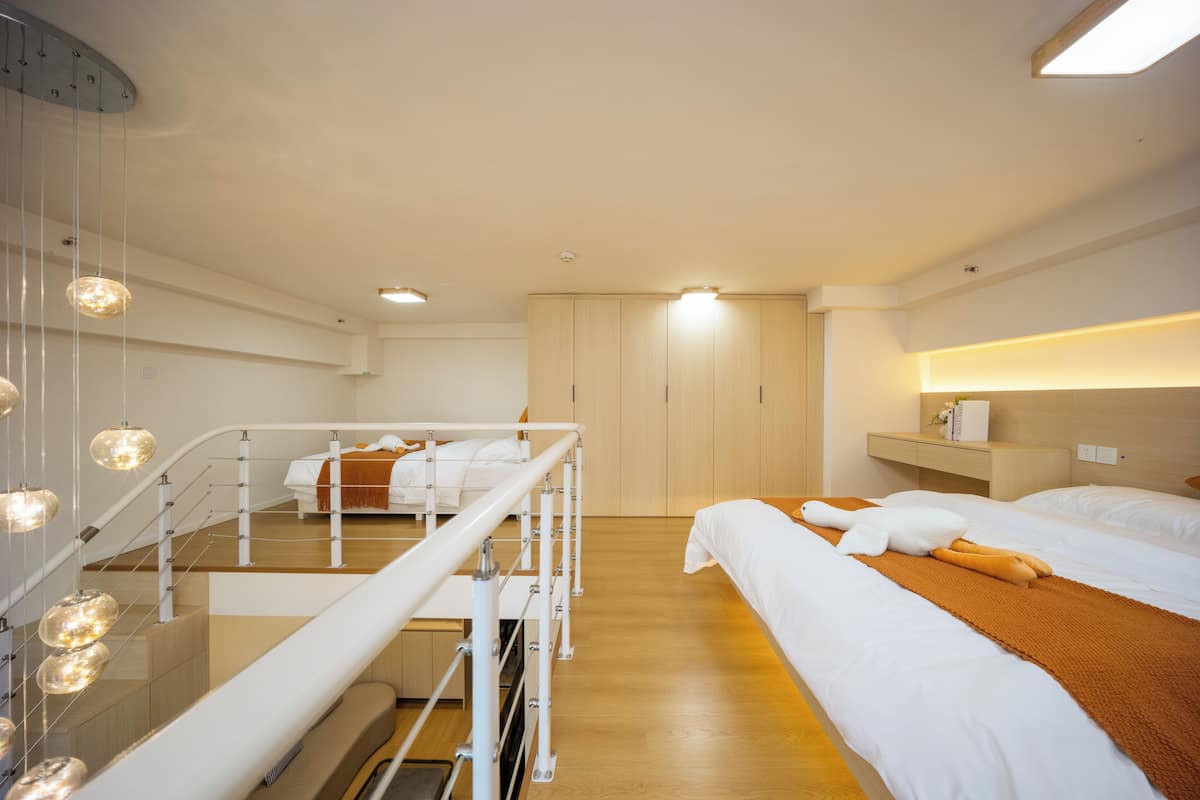 Une chambre d’hôtel avec un escalier, un lit avec une literie blanche, un plaid marron et une table de chevet avec une lampe.