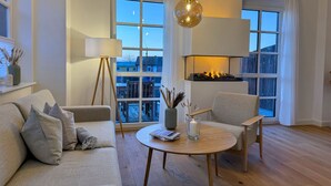A modern living room with a sofa, armchairs, a round coffee table, a floor lamp, and a fireplace. - Pirate ship-private spa, fireplace, sea view & gym (Fehmarn)