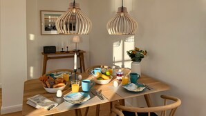 A dining table with breakfast items, two hanging pendant lights, a vase with flowers, and a framed picture on the wall. - Pirate ship-private spa, fireplace, sea view & gym (Fehmarn)