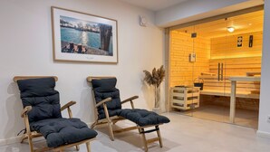 A room with two wooden chairs with cushions, a framed picture on the wall, and a wooden cabinet with a clock. - Pirate ship-private spa, fireplace, sea view & gym (Fehmarn)