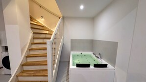 A modern bathroom with a freestanding bathtub, a wooden staircase, and a visible washing machine in the background. - Pirate ship-private spa, fireplace, sea view & gym (Fehmarn)