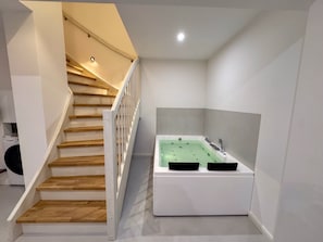 Ein modernes Badezimmer mit einer freistehenden Badewanne, einer Holztreppe und einer sichtbaren Waschmaschine im Hintergrund.