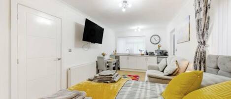 Espai vital compacte amb llit, sofà, televisió plana, zona de cuina i taula de dinar.