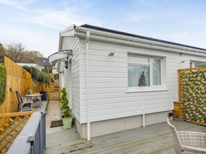 Una casa móvil blanca con una ventana, un patio con mesa y sillas, y una valla de madera.