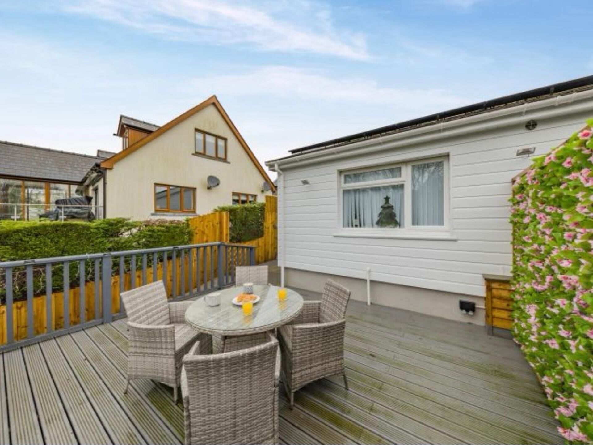 A deck with wicker furniture and a table, surrounded by a wooden fence and a house with white siding.