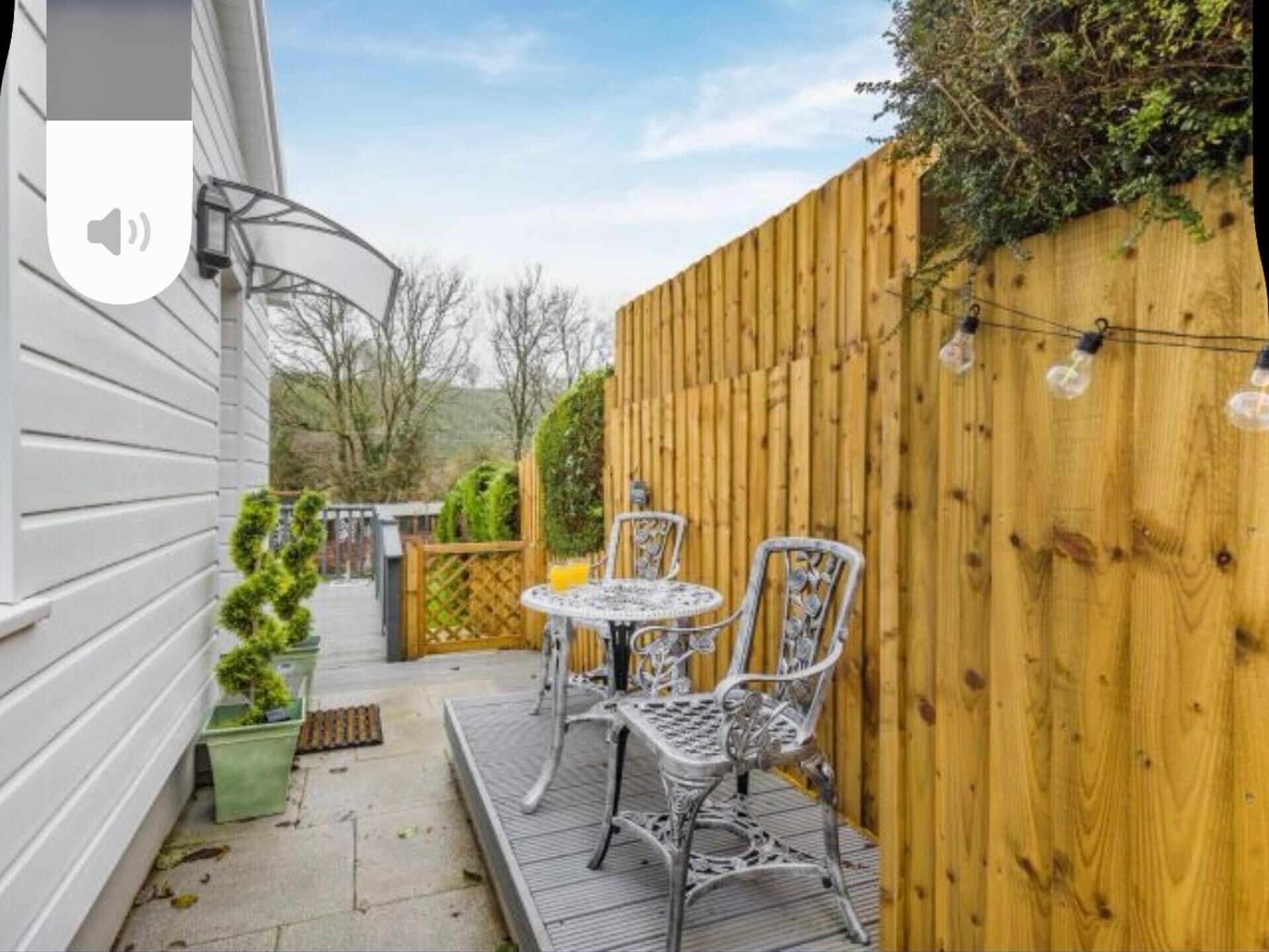 A patio with a table and chairs, a wooden fence, and a speaker mounted on the wall.