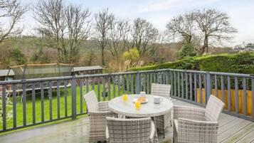 A deck with wicker furniture and a table, surrounded by a wooden fence and trees.