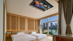 Ein modernes Hotelzimmer mit großem Fenster, zwei Betten, einer Wandpaneele aus Holz und einem digitalen Bildschirm über den Betten.