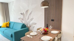 A dining area with a wooden table set for four, a blue sofa with yellow cushions, and a wall with vertical wooden slats. - Villa Nina - apartment Sea view 30 by Villas Guide (Fažana)