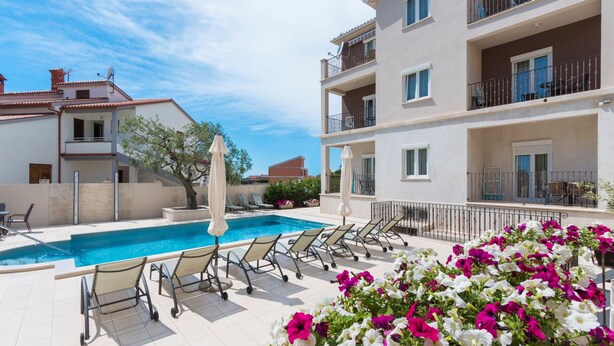 Zona junto a la piscina con sillones, piscina y un edificio con balcones.