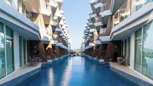 A modern hotel with a central swimming pool, multiple balconies, and large windows. - Beachfront Stay Walk to Beach • Gym • Pool C273 (Rawai)