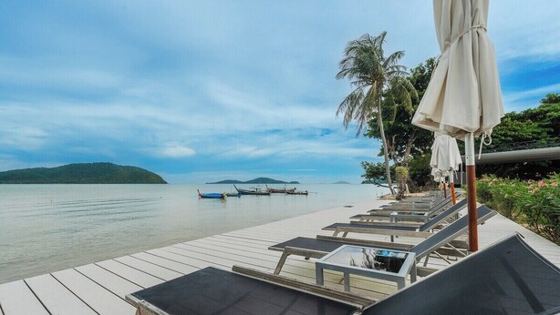 A wooden deck with lounge chairs and umbrellas, overlooking calm water with boats and a distant island. - Beachfront Stay Walk to Beach • Gym • Pool C273 (Rawai)