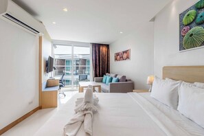 A hotel room with a bed, a sofa, a desk, a chair, and a window. - Beachfront Stay Walk to Beach • Gym • Pool C273 (Rawai)