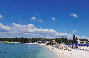 Ein Strand mit einer Bar, blauem Himmel und einem Kiesufer.