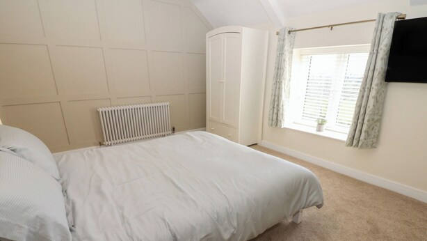 A bedroom with a bed, a radiator, a window with curtains, and a TV mounted on the wall. - 2 Low Road (Bishop Auckland)