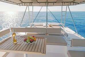 Ein Bootsdeck mit gedecktem Tisch für eine Mahlzeit, darunter eine Flasche, Gläser und eine Schüssel mit Obst.