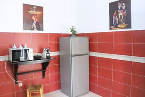 Eine Küche mit Kühlschrank, Mikrowelle und Toaster auf einem schwarzen Regal, roten Fliesenwänden und zwei gerahmten Bildern über der Arbeitsplatte.