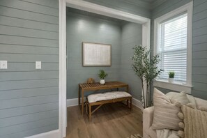 A room with light gray walls, a wooden bench with cushions, a framed picture on the wall, and a window with blinds. - Luxury Stay • Near Heights, Galleria & Downtown (Houston)