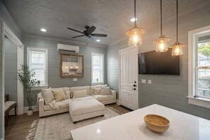 A room with a sectional sofa, a dining table, pendant lights, a ceiling fan, an air conditioning unit, a large mirror, and a TV mounted on the wall. - Luxury Stay • Near Heights, Galleria & Downtown (Houston)