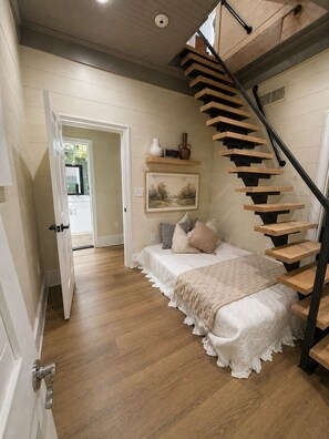 A bedroom with a wooden staircase, a bed with a white bedspread, and a painting on the wall. - Luxury Stay • Near Heights, Galleria & Downtown (Houston)