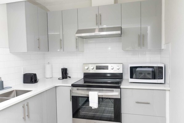 Cozinha com armários brancos, forno de aço inoxidável, micro-ondas e torradeira.