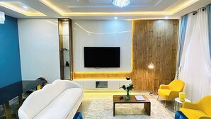 Una sala de estar moderna con un televisor de pantalla plana grande, un sofá blanco, un sofá azul y sillones amarillos.