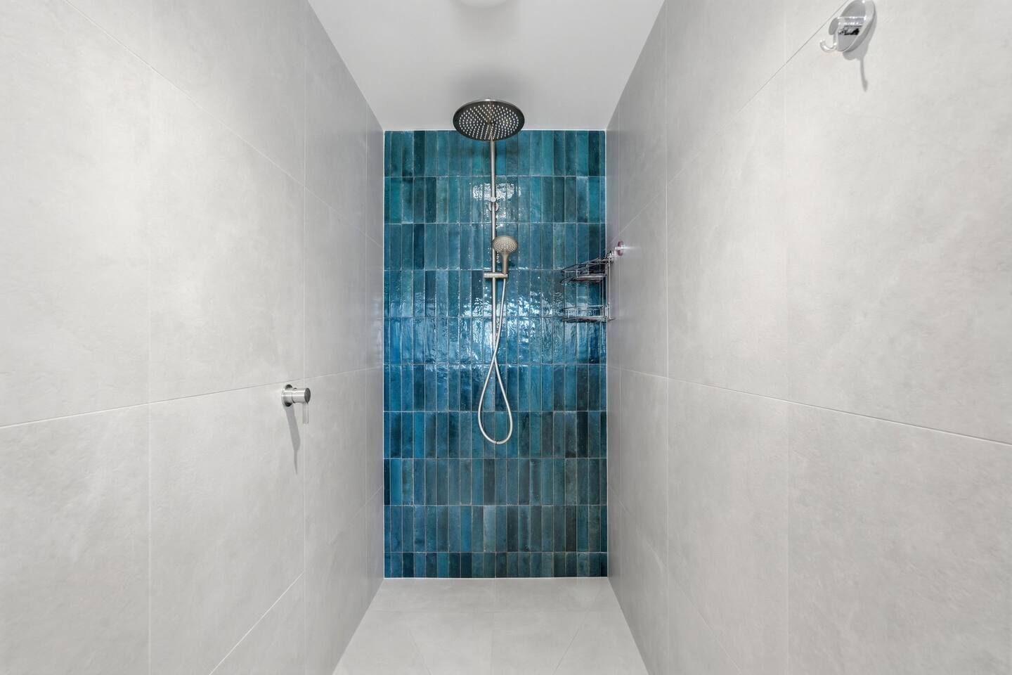 A narrow shower area with a blue-tiled wall, a handheld showerhead, and a wall-mounted faucet.