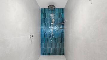 A narrow shower area with a blue-tiled wall, a handheld showerhead, and a wall-mounted faucet.