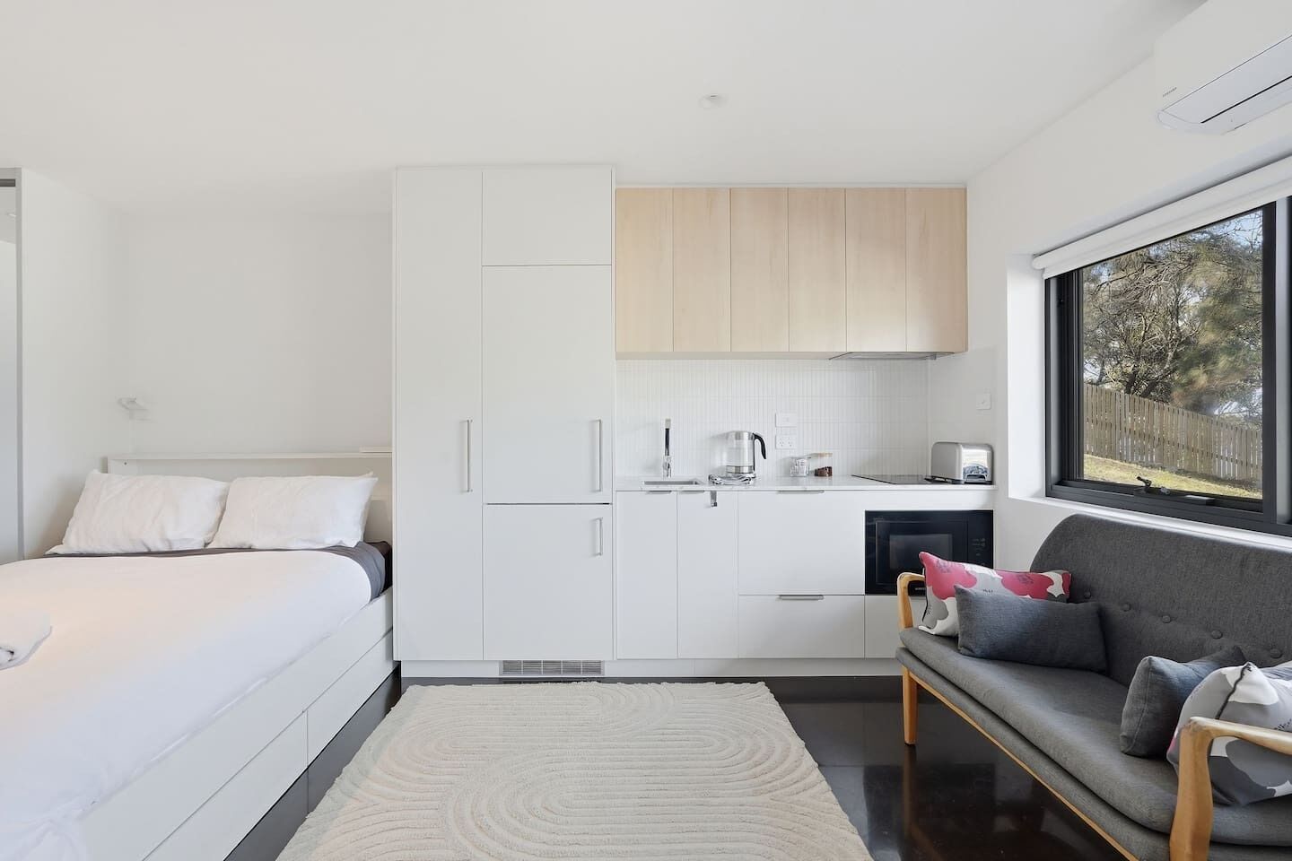 Une chambre moderne comprenant un lit, un canapé, un coin cuisine et une fenêtre donnant sur un paysage agréable.