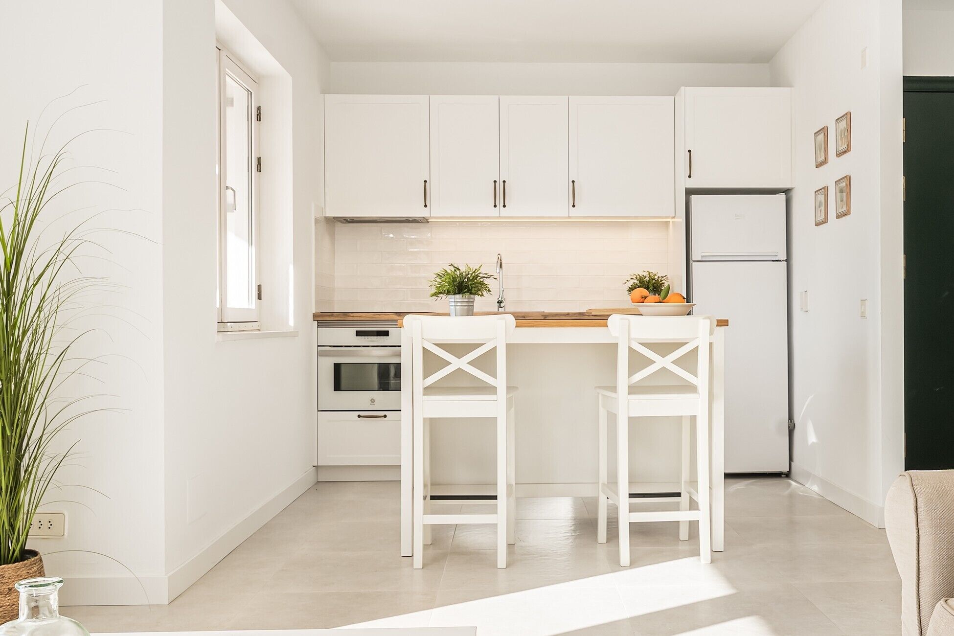 Una cocina moderna con armarios blancos, encimera de madera, dos taburetes blancos y un refrigerador.