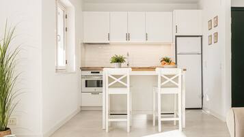 Una cocina moderna con armarios blancos, encimera de madera, dos taburetes blancos y un refrigerador.