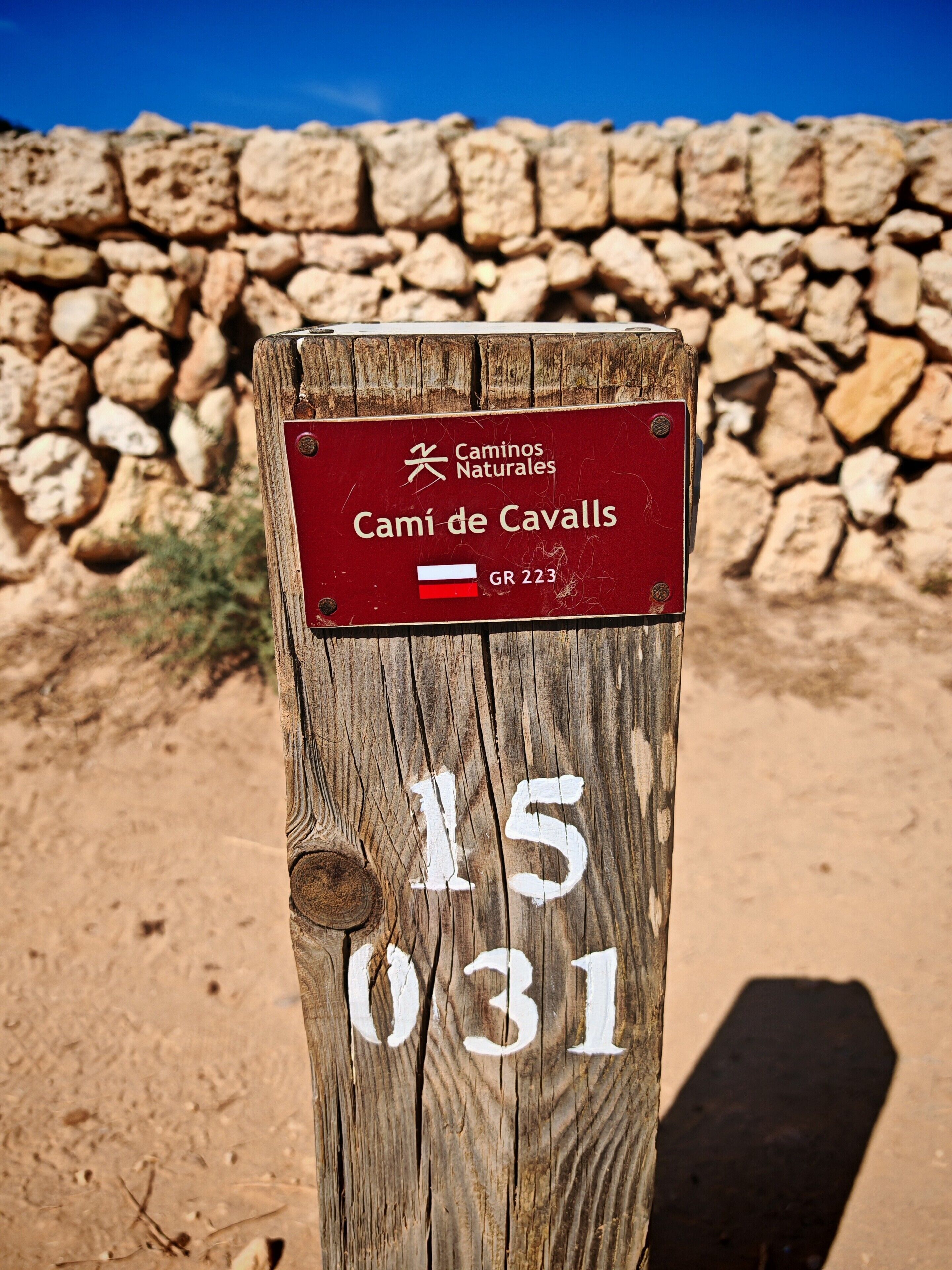 A wooden post with a red sign indicating 'Camí de Cavalls' and a route number 'GR 223'.