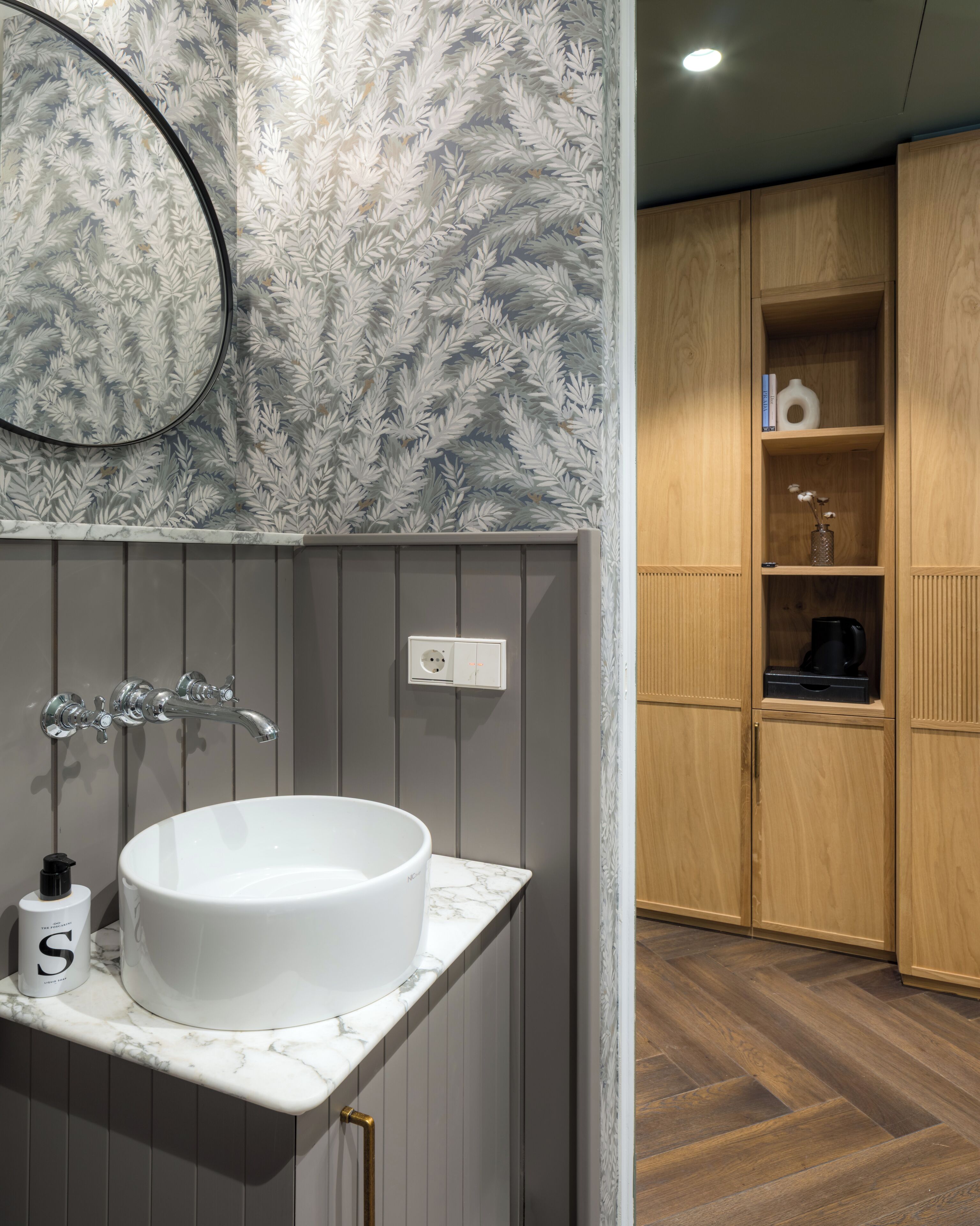 A bathroom with a white sink, a mirror, and a frosted leaf-patterned wall.