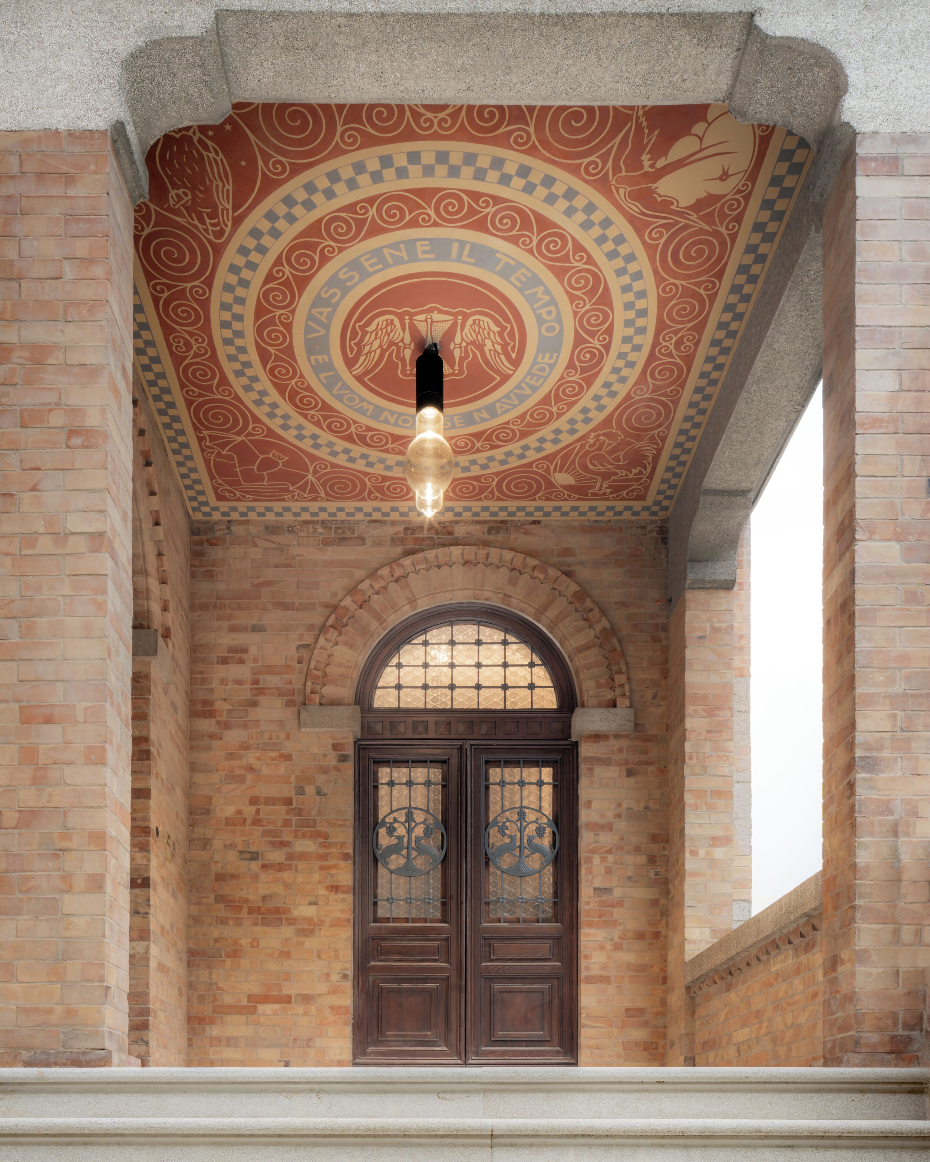 Un edificio con fachada de ladrillo, techo decorativo y puerta doble con ornamentación metálica detallada.