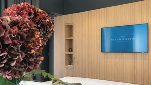 A modern hotel room with a bed, a television, a wooden panel wall, and a vase with flowers. - The Castelletto (Montebelluna)